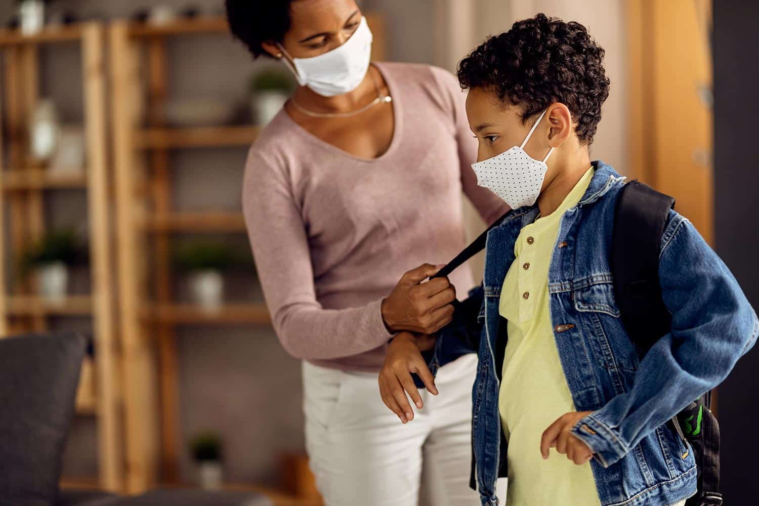 Black mother and son with face masks preparing to go back to school during coronavirus pandemic