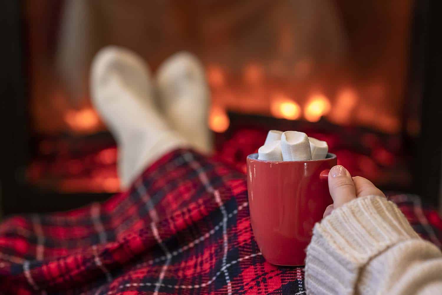 woman with hot cocoa at fireplace