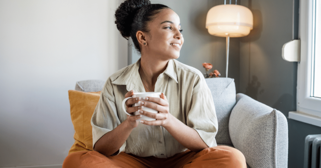 A woman smiling and looking out the window while holding a cup of coffee.